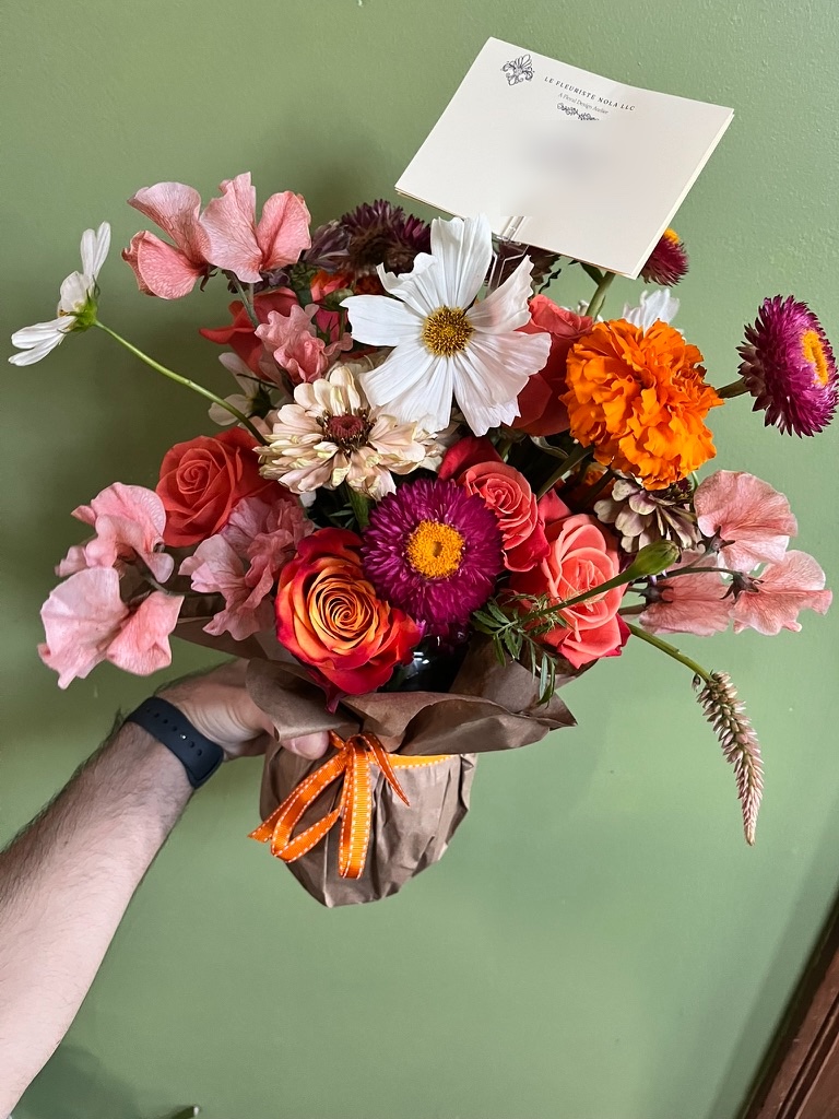 Hand-tied bouquet of garden roses, cosmos, sweet peas, and marigold wrapped in kraft paper