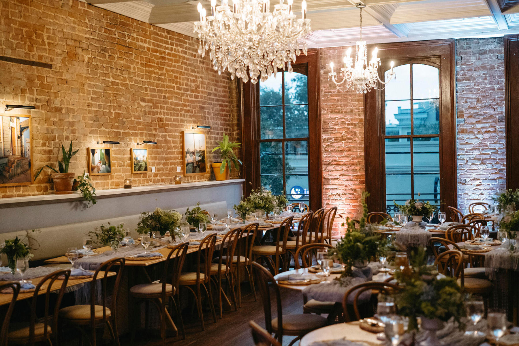 Long dinner tables with low garden arrangements in a brick-walled dining room