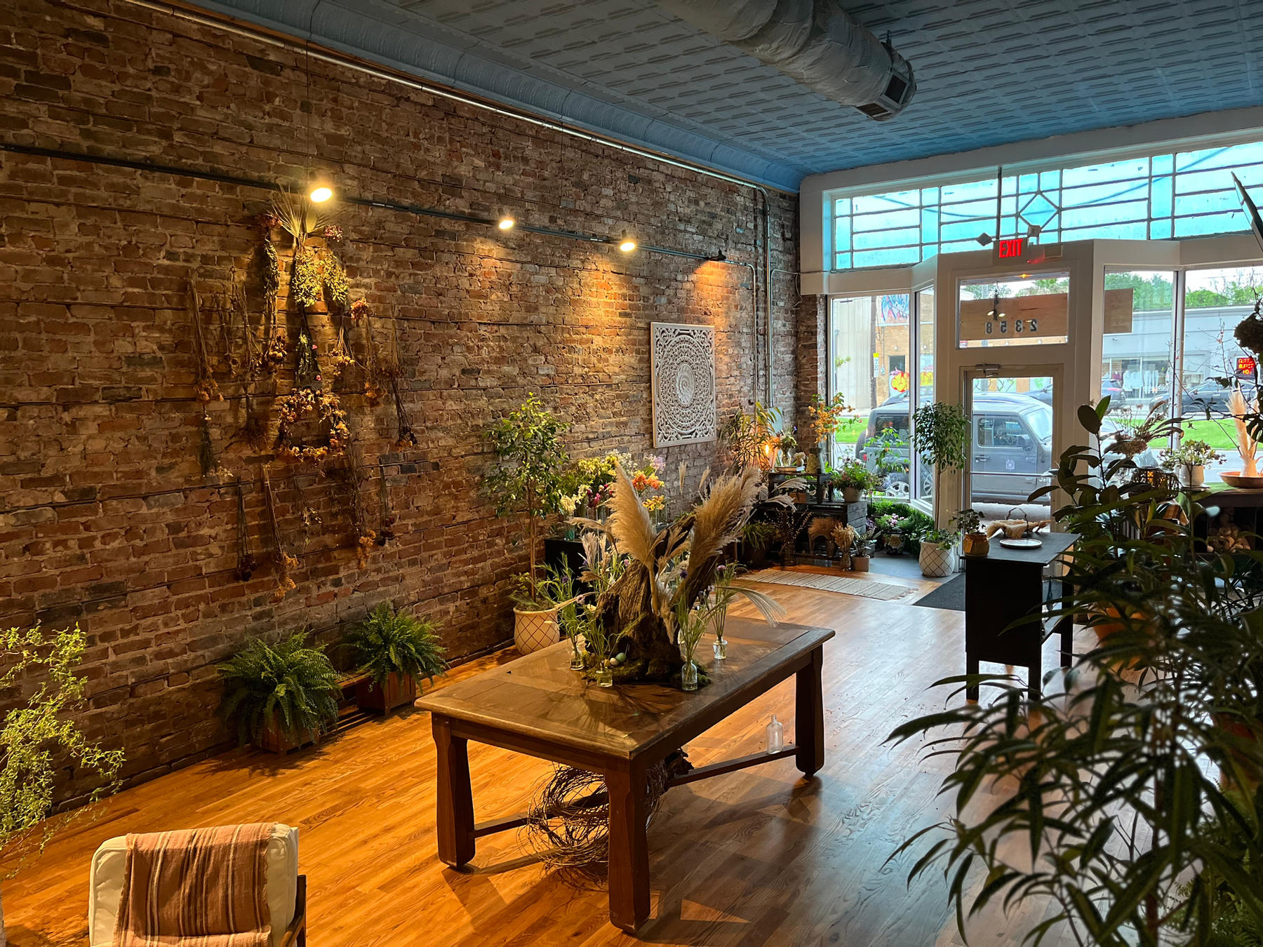 The studio: dried flowers hung along a brick wall, a worktable and greenery